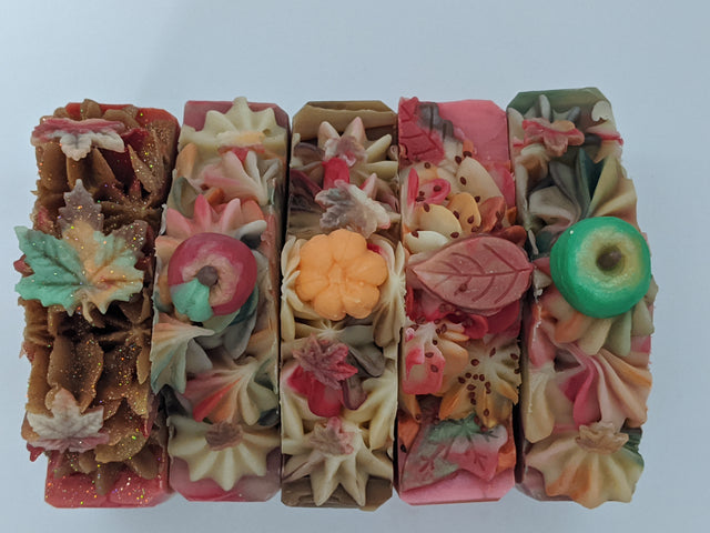 All The Way Handmade by Sienna frosted soap collection. Beautiful handmade cold process soap fall collection with leaves, pumpkins, and apples. Soaps lined up on their side with soap embeds. The soaps are autumn colors and smell amazing!